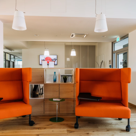 Moderne und einladende Büroecke mit orangefarbenen Sofas und einer stilvollen Beleuchtung in der Waagner-Biro-Straße 47, perfekt um einen Büroraum zu mieten.