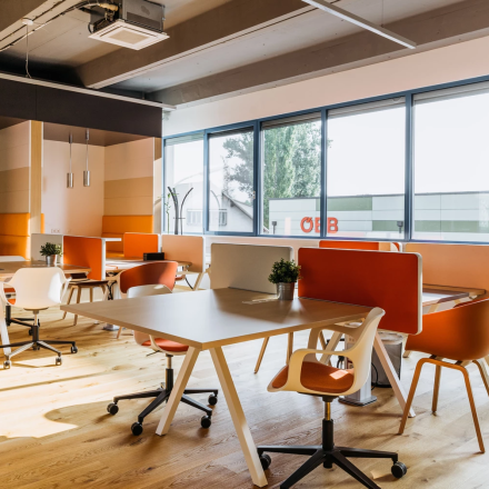 Modern gestalteter Büroraum mieten in Graz, Waagner-Biro-Straße 47, mit Holzboden, Schreibtischen und orangen Stühlen.
